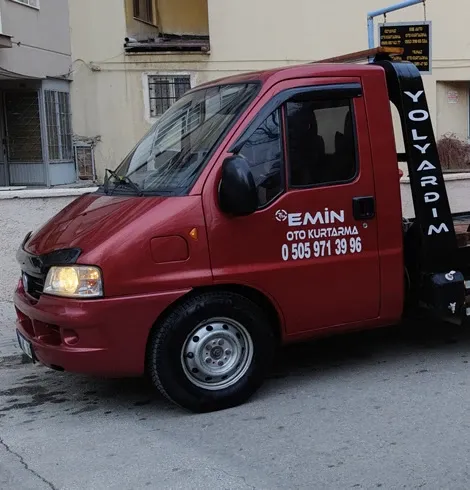 Kapısında Emin Oto Kurtarma ve 0 505 971 39 96 yazan, sokakta park halindeki kırmızı çekici