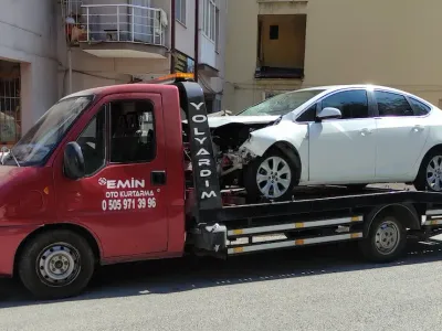 Apartman önünde ön tarafı kazada hasar görmüş beyaz sedanı taşıyan Emin Oto Kurtarma çekicisi