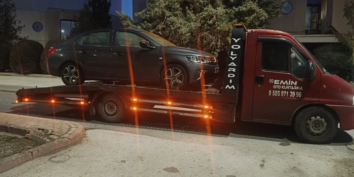 Gece bir bina önünde koyu gri sedanı kasasına almış Emin Oto Kurtarma kayar kasalı çekicisi