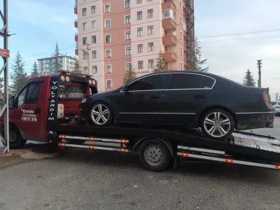 Yüksek apartman blokları önünde siyah sedan otomobili taşıyan Emin Oto Kurtarma çekicisi