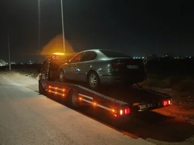 Gece ıssız bir yol kenarında gri sedan otomobili kasasına yüklemiş kayar kasalı çekici, arkadan görünüm
