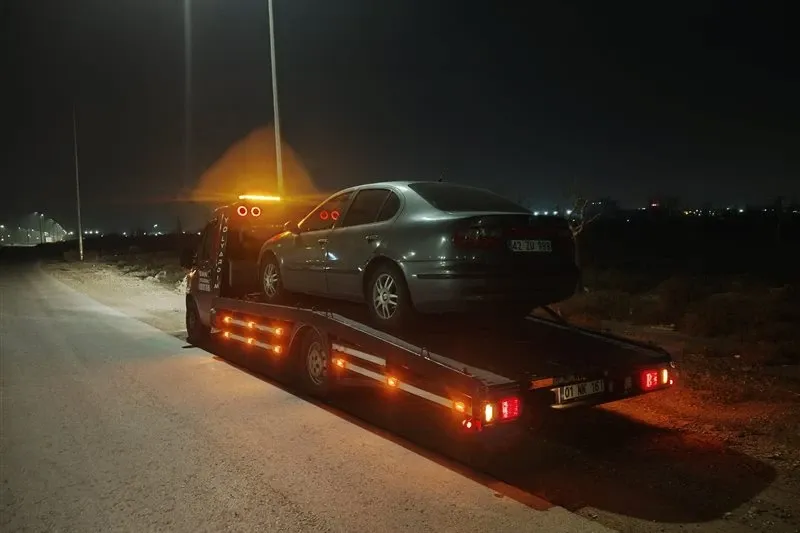 Gece ıssız bir yol kenarında gri sedan otomobili kasasına yüklemiş kayar kasalı çekici, arkadan görünüm