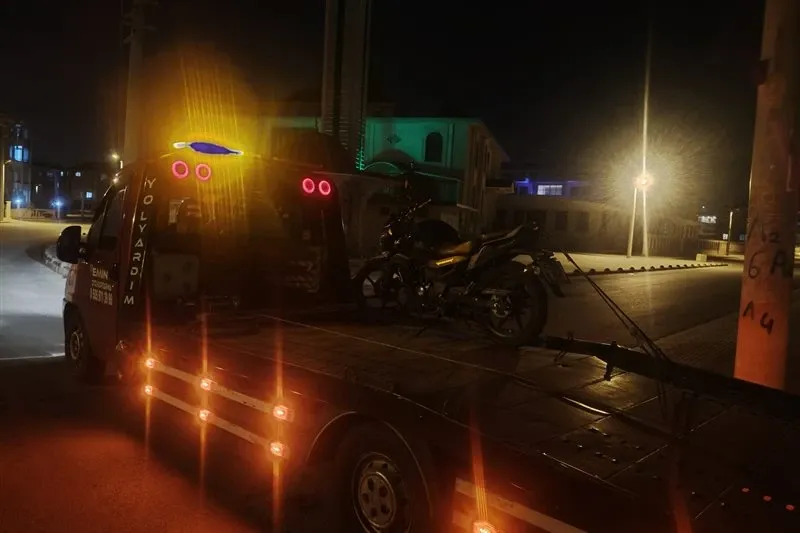 Gece şehir içinde Emin Oto Kurtarma çekicisinin kasasına kayışlarla sabitlenmiş siyah motosiklet