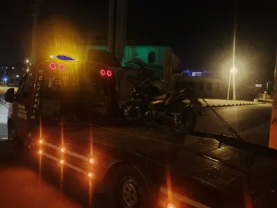 Gece şehir içinde Emin Oto Kurtarma çekicisinin kasasına kayışlarla sabitlenmiş siyah motosiklet