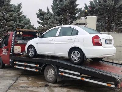 Islak zeminde kasası arkaya yatırılmış Emin Oto Kurtarma kayar kasalı çekicisine yüklenmiş beyaz sedan