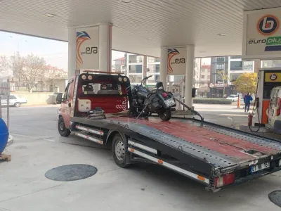 Akaryakıt istasyonunda kasası eğik kayar kasalı çekiciye yüklenip sabitlenmiş siyah motosiklet