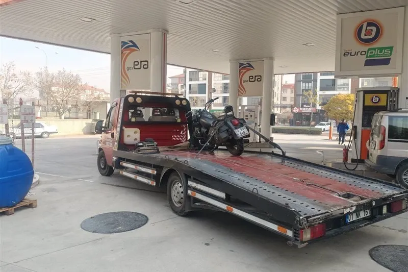 Akaryakıt istasyonunda kasası eğik kayar kasalı çekiciye yüklenip sabitlenmiş siyah motosiklet