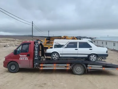 Sarı iş makinelerinin çalıştığı şantiye alanında klasik beyaz sedanı taşıyan Emin Oto Kurtarma çekicisi