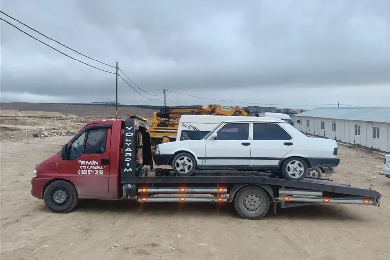 Sarı iş makinelerinin çalıştığı şantiye alanında klasik beyaz sedanı taşıyan Emin Oto Kurtarma çekicisi