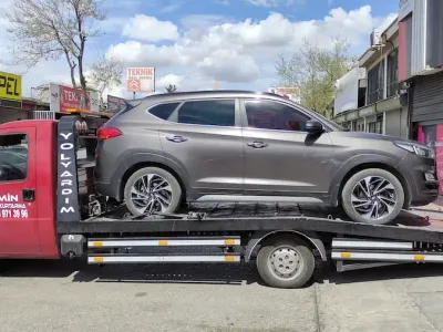 Yedek parça dükkânlarının sıralandığı sokakta gri SUV'u taşıyan Emin Oto Kurtarma çekicisi