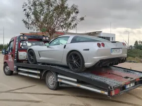 Bulutlu havada yol kenarında gümüş renkli spor otomobili taşıyan Emin Oto Kurtarma çekicisi