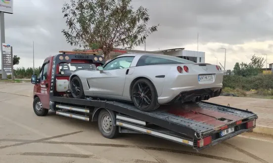 Bulutlu havada yol kenarında gümüş renkli spor otomobili taşıyan Emin Oto Kurtarma çekicisi